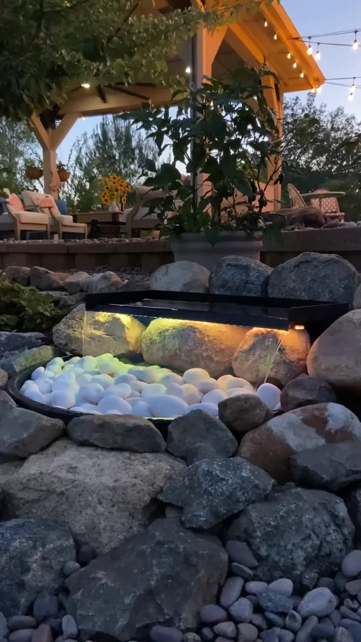 A glowing waterfall beside rustandseed's backyard seating corner at dusk
